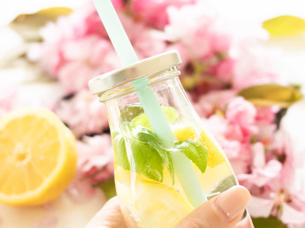 A bottle of lemon and mint water held up against pink blossom.